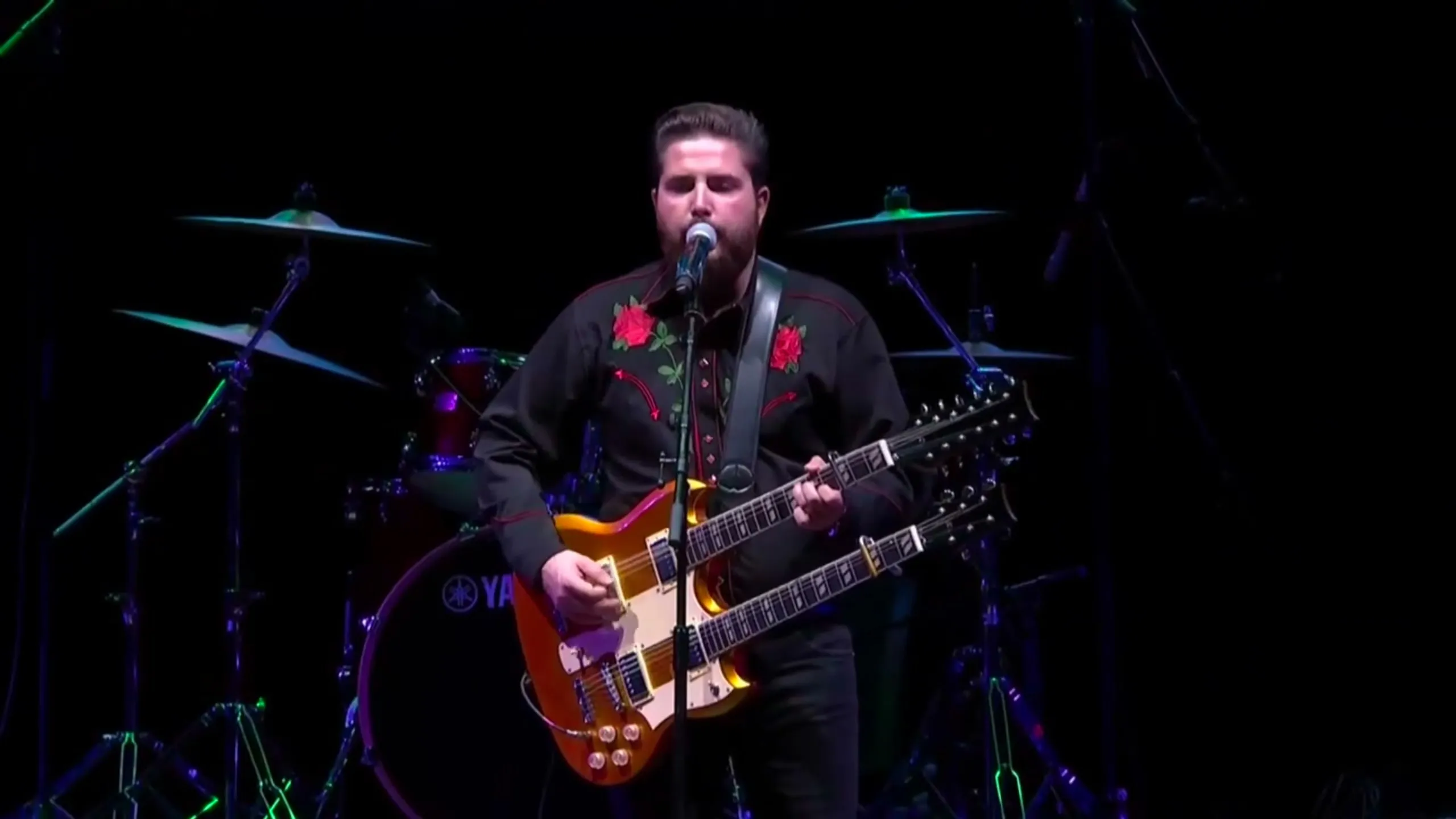 JJ Fuentes cantando con una guitarra de doble mástil en el escenario del WiZink Center, con la batería detrás